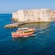 A wooden tour boat sailing past the stone fortress entrance of Dubrovnik's Old Port